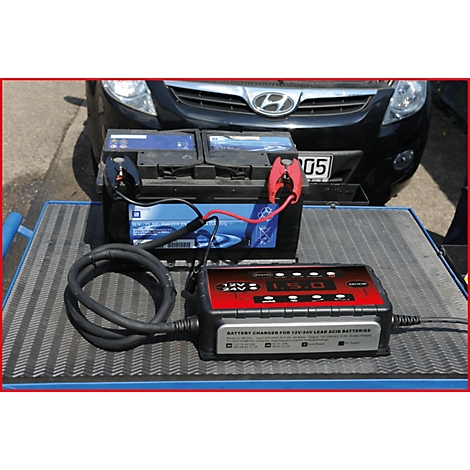 Batterieladegerät lädt Autobatterie. Rote und schwarze Kabel verbunden, Ladegerät mit Anzeige.